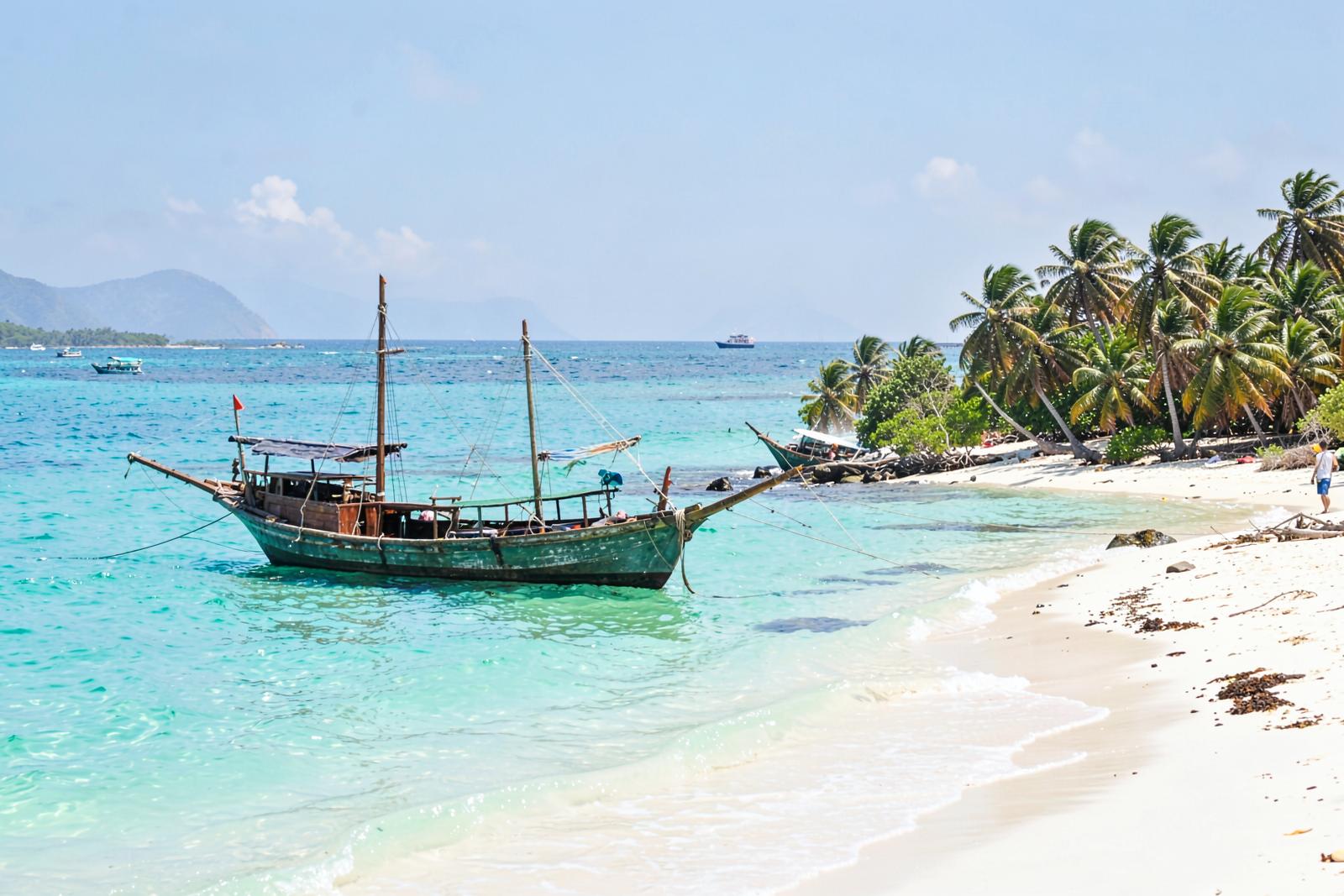 Traditional wooden dhow moored on a turquoise Zanzibar beach lined with palms